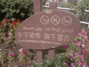 Park sign in Urumqi: "Please Show Mercy to Grass and Flowers," in English, Mandarin, and Uyghur languages.